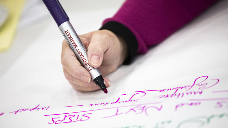 A person holds a pen which has just written 'Next Steps'